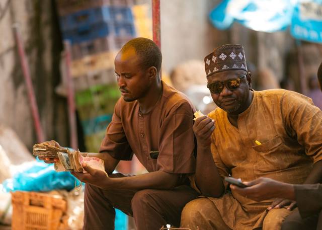 Two traders in a market counting naira notes together