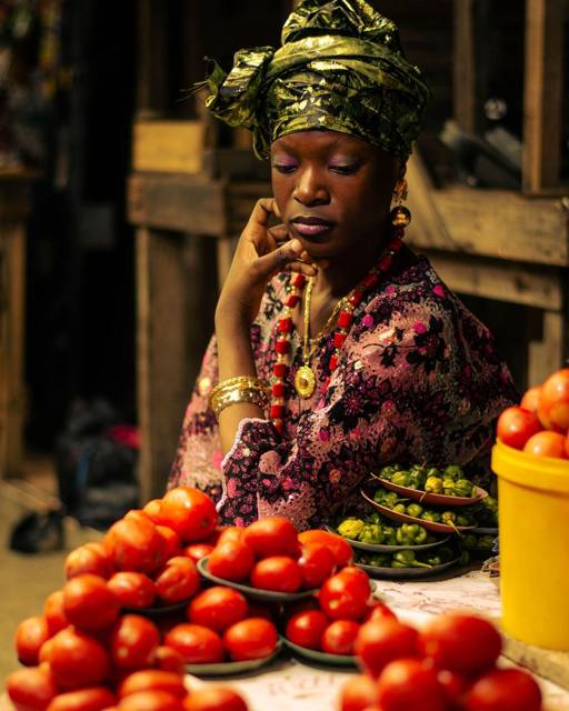A trader with fresh tomatoes and peppers arranged on her stall